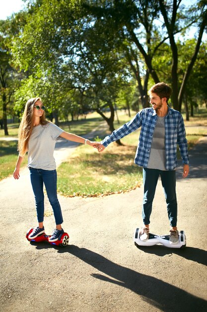 Photo young man and woman riding on the hoverboard in the park content technologies a new movement