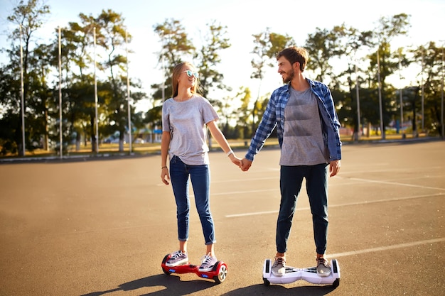 Photo young man and woman riding on the hoverboard in the park content technologies a new movement