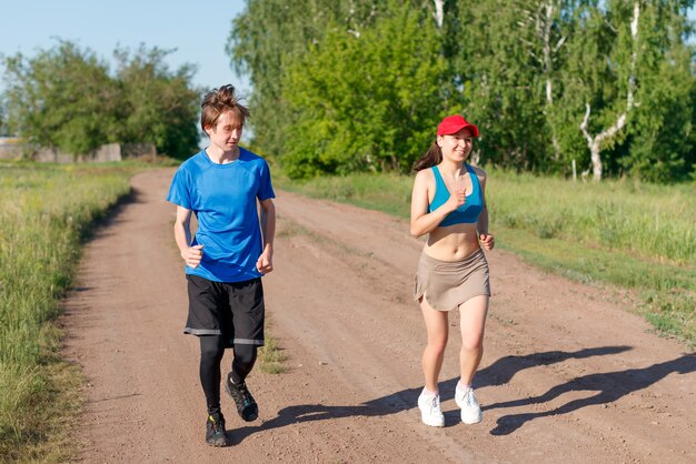 A young man and a woman run together outdoors in the summer