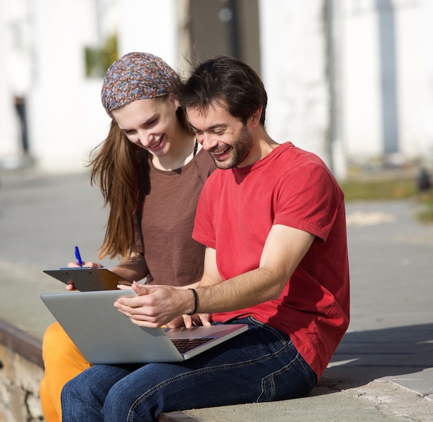 Young man and woman smiling at laptop outdoors 