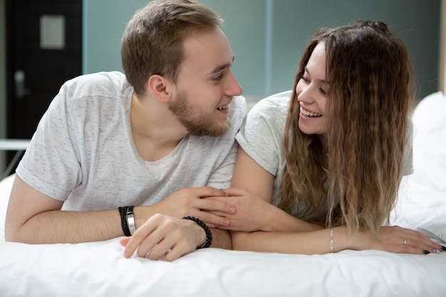 Young man and woman, something fun to discuss with each other lying on the bed and holding hands