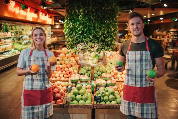 Young man and woman stand at fruit boxes in grocery store