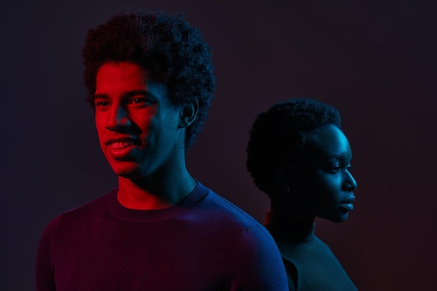 Young man and woman standing together in neon light over dark background, concept of human emotions, facial expression, fashion, beauty