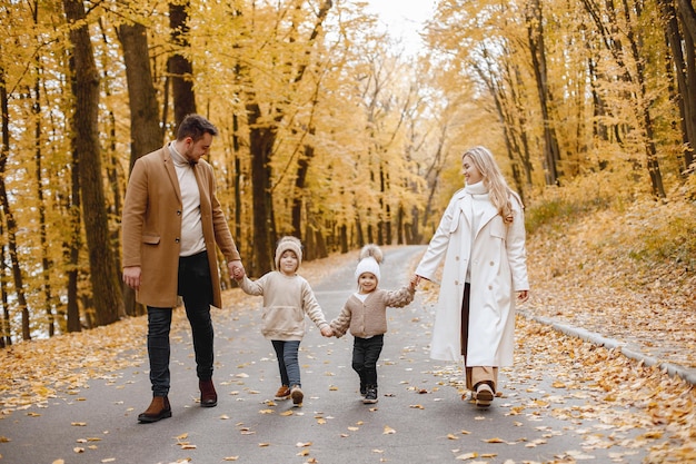 Young man, woman and their children walking outside wearing beige coats. Blond mother, brunette father, little girl and boy holding hands. Parents wearing coats, children - hats.