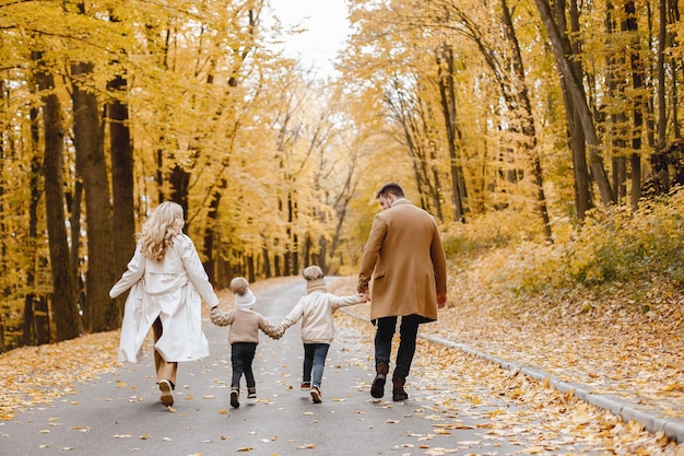 Young man, woman and their children walking outside wearing beige coats. Blond mother, brunette father, little girl and boy holding hands. Parents wearing coats, children - hats.