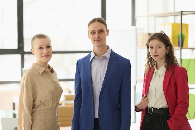 Young man and women in formal outfits look in camera standing against bright window successful