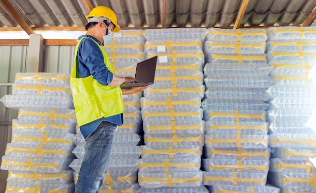 Young man worker  using laptop checking number of white plastic bottles in the warehouse