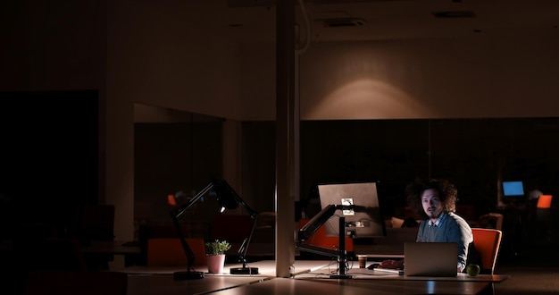 Young man working on computer at night in dark office. The designer works in the later time.