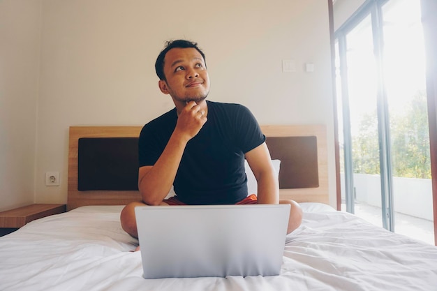 Young man working from the bed pondering while looking aside