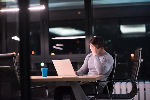 Young man working on laptop at night in dark office. The designer works in the later time.