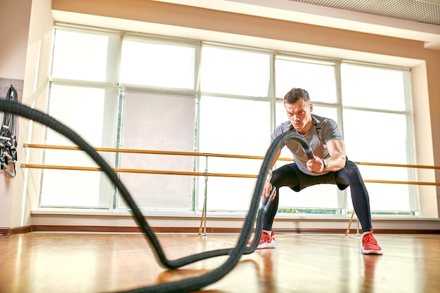 Young man working out with battle ropes at a gym