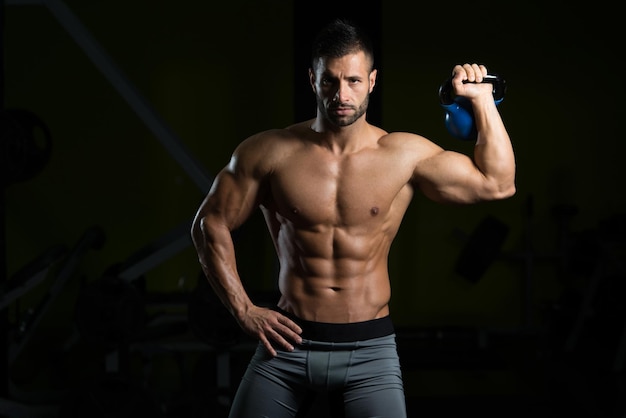 Young Man Working Out With Kettle Bell In A Dark Gym  Bodybuilder Doing Heavy Weight Exercise With Kettlebell