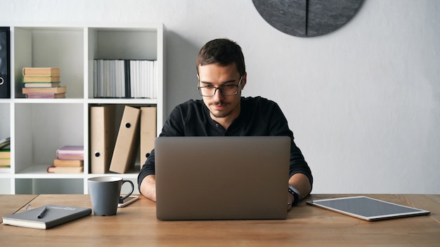 Young man working with computer phone and tablet at the table while drinking coffee