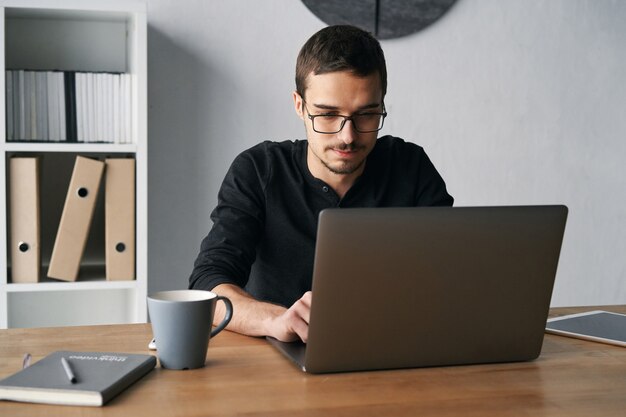 Young man working with computer phone and tablet at the table while drinking coffee