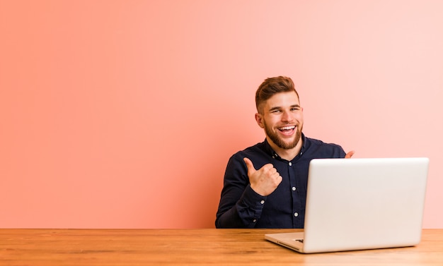 Young man working with his laptop raising both thumbs up, smiling and confident.