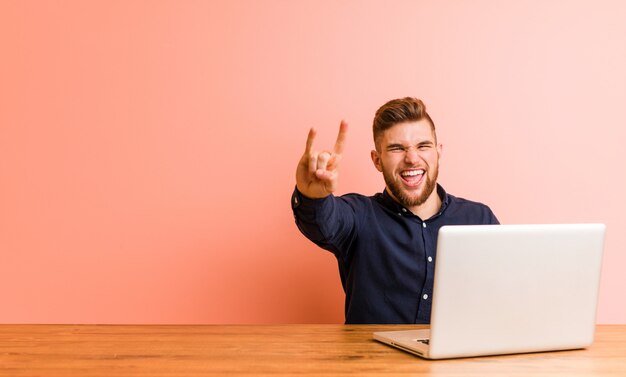 Young man working with his laptop showing a horns gesture as a revolution concept.