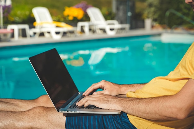 Young man working with laptop next to the pool during a sunny day attractive man working freelancer