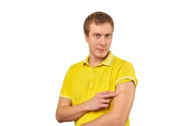 Young man in yellow Tshirt showing plaster on shoulder after coronavirus vaccination isolated