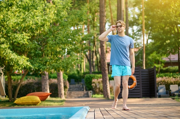 A young man. A young man in a blue tshirt and sunglasses near swimming pool