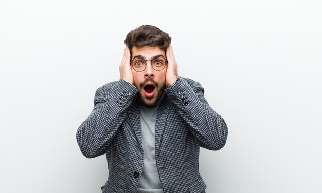 Photo young manager man looking unpleasantly shocked, scared or worried, mouth wide open and covering both ears with hands against white wall