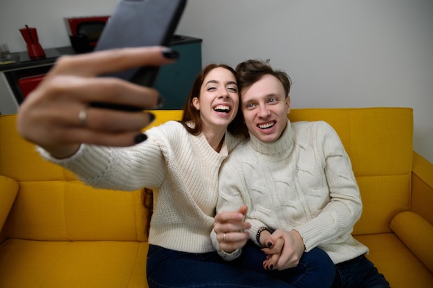 A young married couple at home they sit on the couch and take selfies