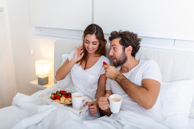 Young married couple in love eating breakfast in their bed Good morning Healthy breakfast in bed Young beautiful love couple is having breakfast in bed