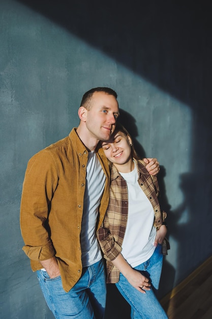 A young married couple in love in shirts and jeans on the background of a gray wall The concept of happy family relationships A man and a woman are hugging