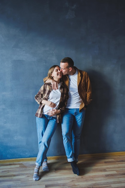 A young married couple in love in shirts and jeans on the background of a gray wall The concept of happy family relationships A man and a woman are hugging