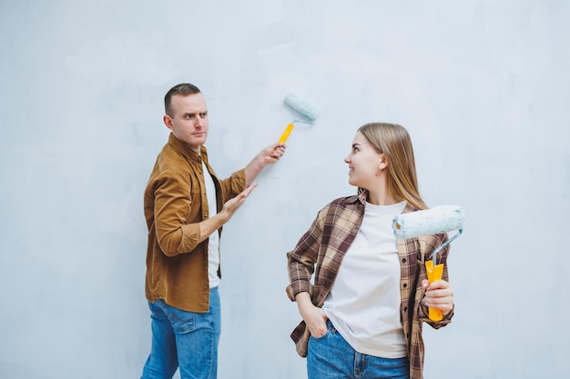 Young married couple in love in shirts and jeans doing renovations renewing painting walls with a roller preparing to move into a new house selective focus