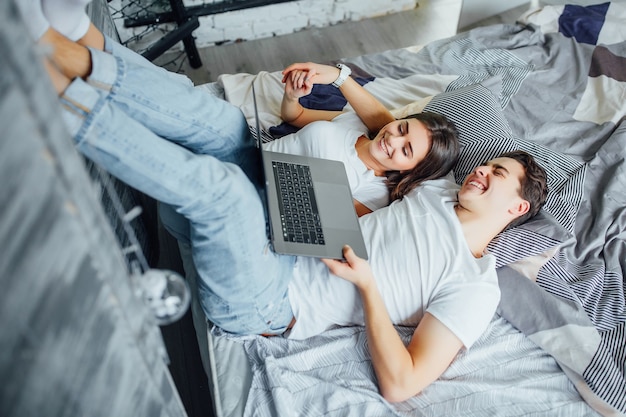 Young married couple lying on bed at home and using laptop. Perfect morning