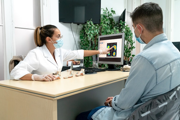 A young masked podiatrist explaining the diagnosis to a patient