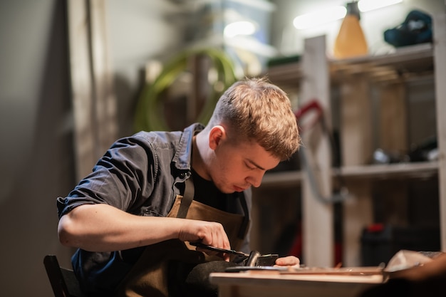 A young master in the manual production of shoes in his workshop is working on creating shoes.