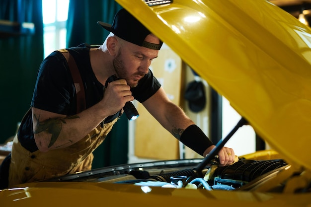 Young mechanic of car repair workshop checking engine of yellow automobile