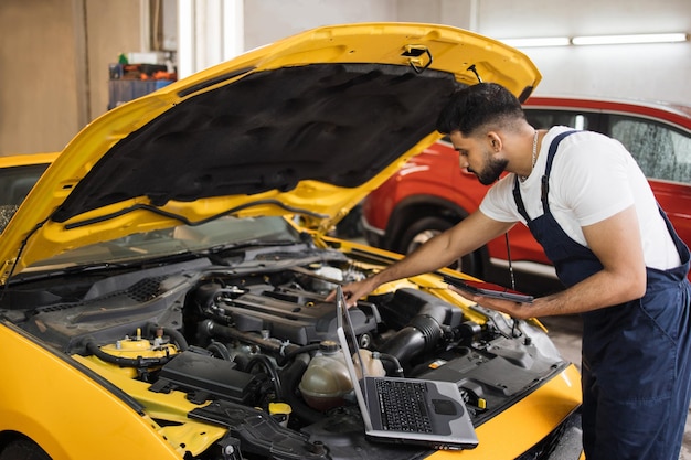 Young mechanic using tablet recording automobile engine checks collect detailed information