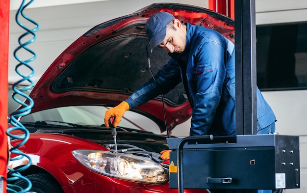 Young mechanik adjusting the headlights on the red modern car in auto service