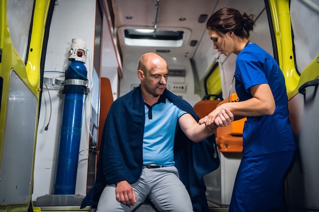 A young medical worker checking the traumatized hand of her patient in an ambulance car.