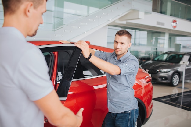 Young men stand by red car and hold its front door opened