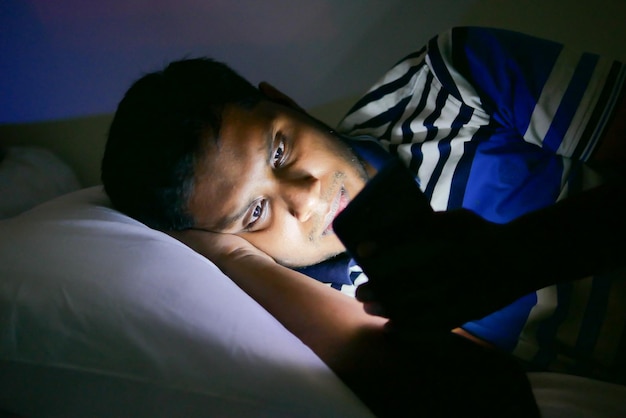 Young men using smart phone on bed at night