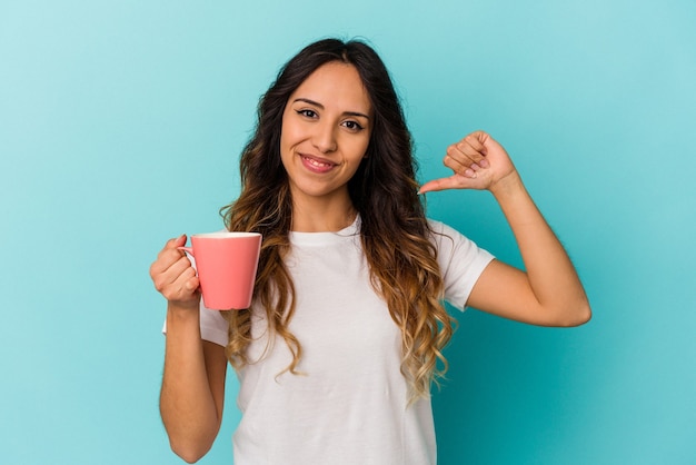 Young mexican woman holding a mug isolated on blue background feels proud and self confident, example to follow.