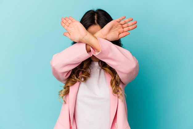 Young mexican woman isolated on blue wall keeping two arms crossed, denial concept.