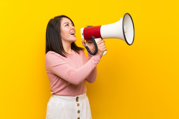 Young Mexican woman over isolated yellow background shouting through a megaphone