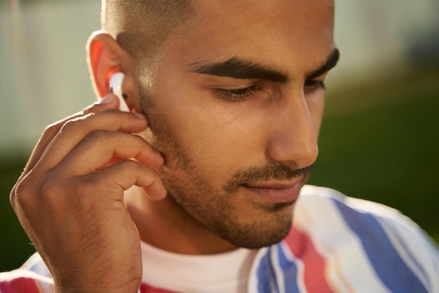 Young middle eastern man listening music wearing wireless earbuds sitting on the street