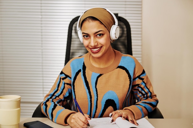 Young Middle Eastern woman wearing headphones in office and smiling at camera