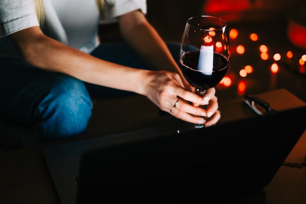 Young millennial woman having video call on laptop computer and drinking wine, use technology for communicate with friends or family.