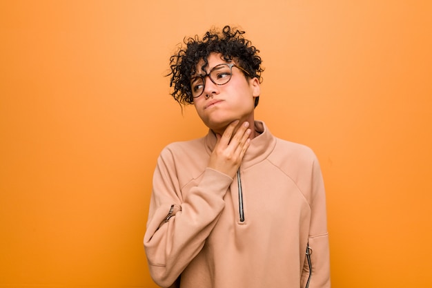 Young mixed african american woman against a brown wall suffers pain in throat due a virus or infection.