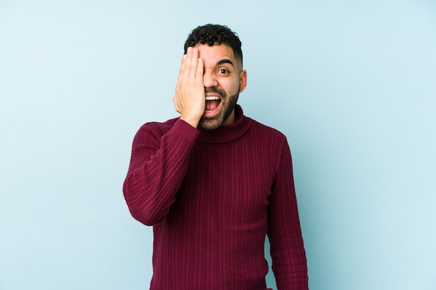 Young mixed race arabic man isolated having fun covering half of face with palm.