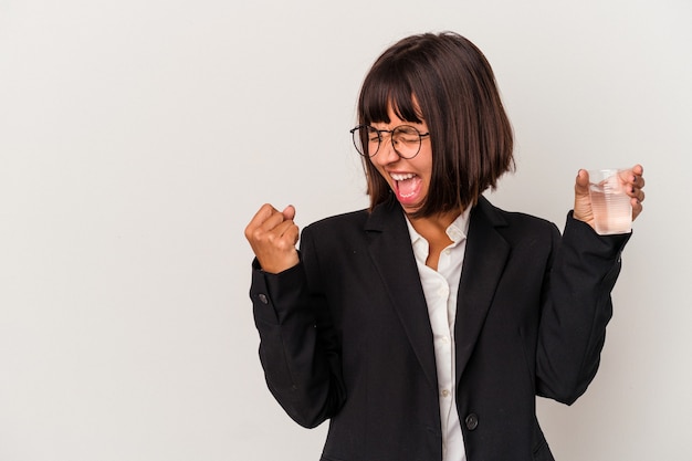 Young mixed race business woman holding a glass of water isolated on white background raising fist after a victory, winner concept.