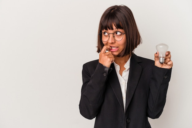 Young mixed race business woman holding a light bulb isolated on white background relaxed thinking about something looking at a copy space.