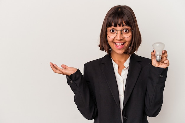 Young mixed race business woman holding a light bulb isolated on white background showing a copy space on a palm and holding another hand on waist.