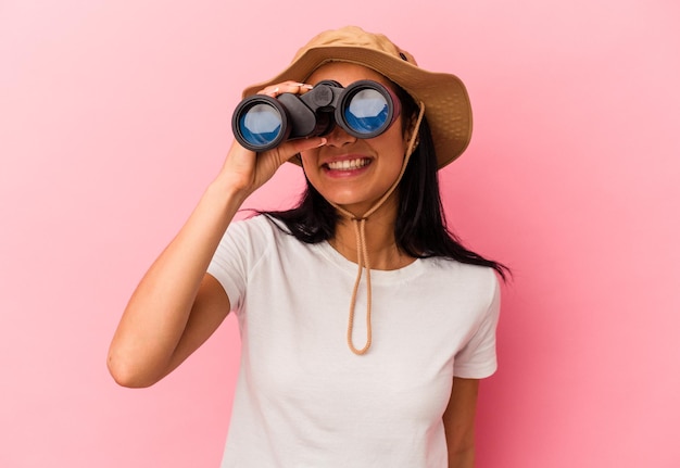 Young mixed race explorer woman holding binoculars isolated on pink background